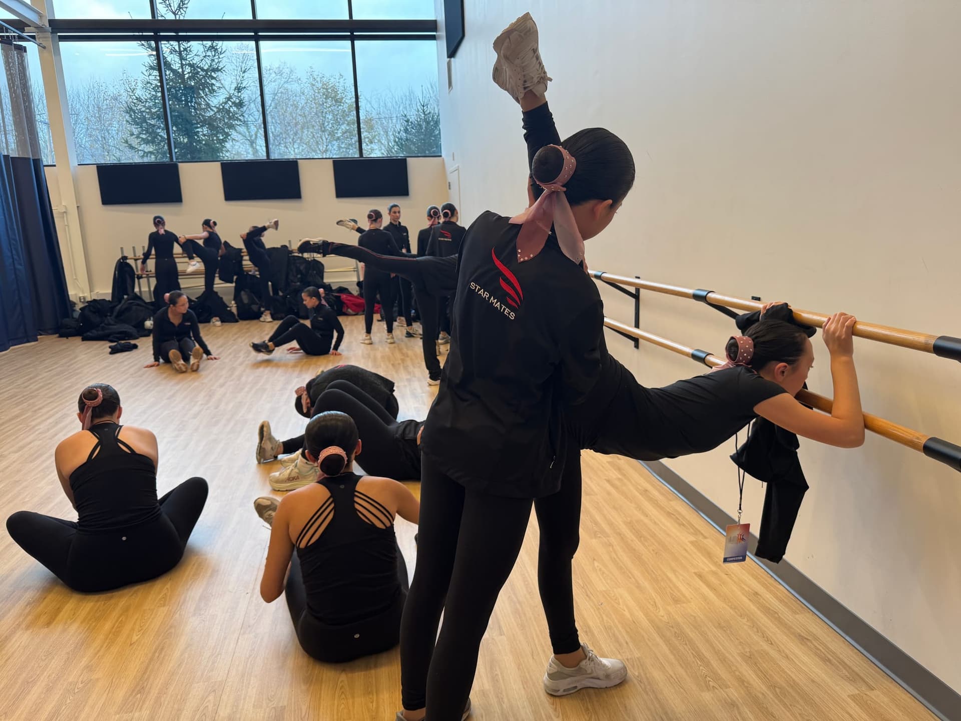 A Star Mates skater stretches at the barre with a teammate during off-ice training, as others warm up behind them